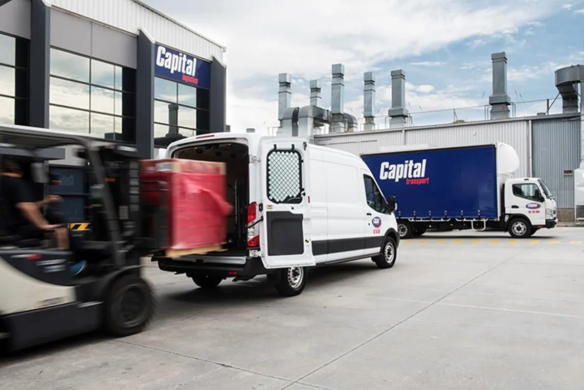 A forklift unloading goods from a white van with a blue Capital Transport Group truck in the background.