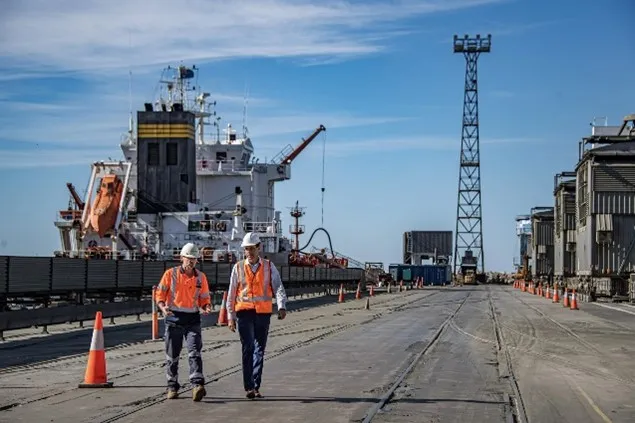 PKG workers in hard hats and hi-vis orange vests on a stevedoring dock next to a cargo ship. The image represents how PKG, a busy port terminal, transformed its induction process.